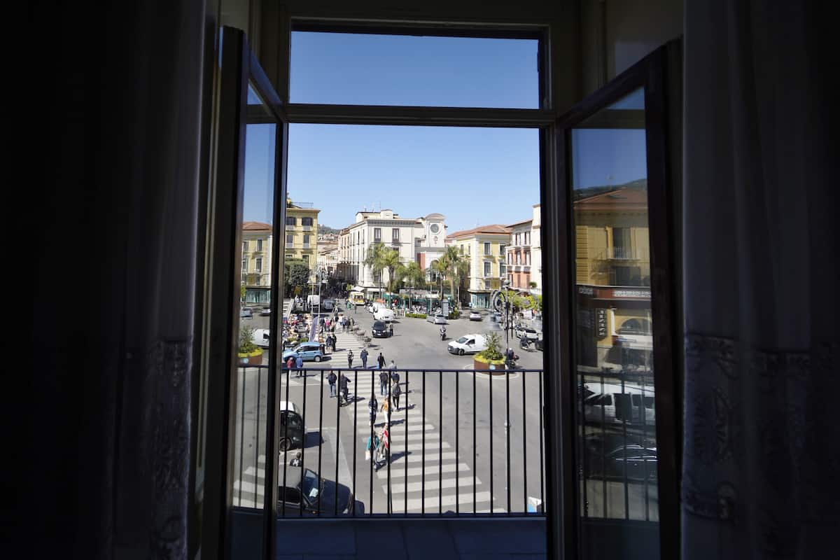 Vista desde un balcón con barandilla, sobre una calle concurrida con edificios y coches.