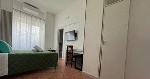 Un dormitorio con cama, una silla, un televisor montado en la pared y un armario.