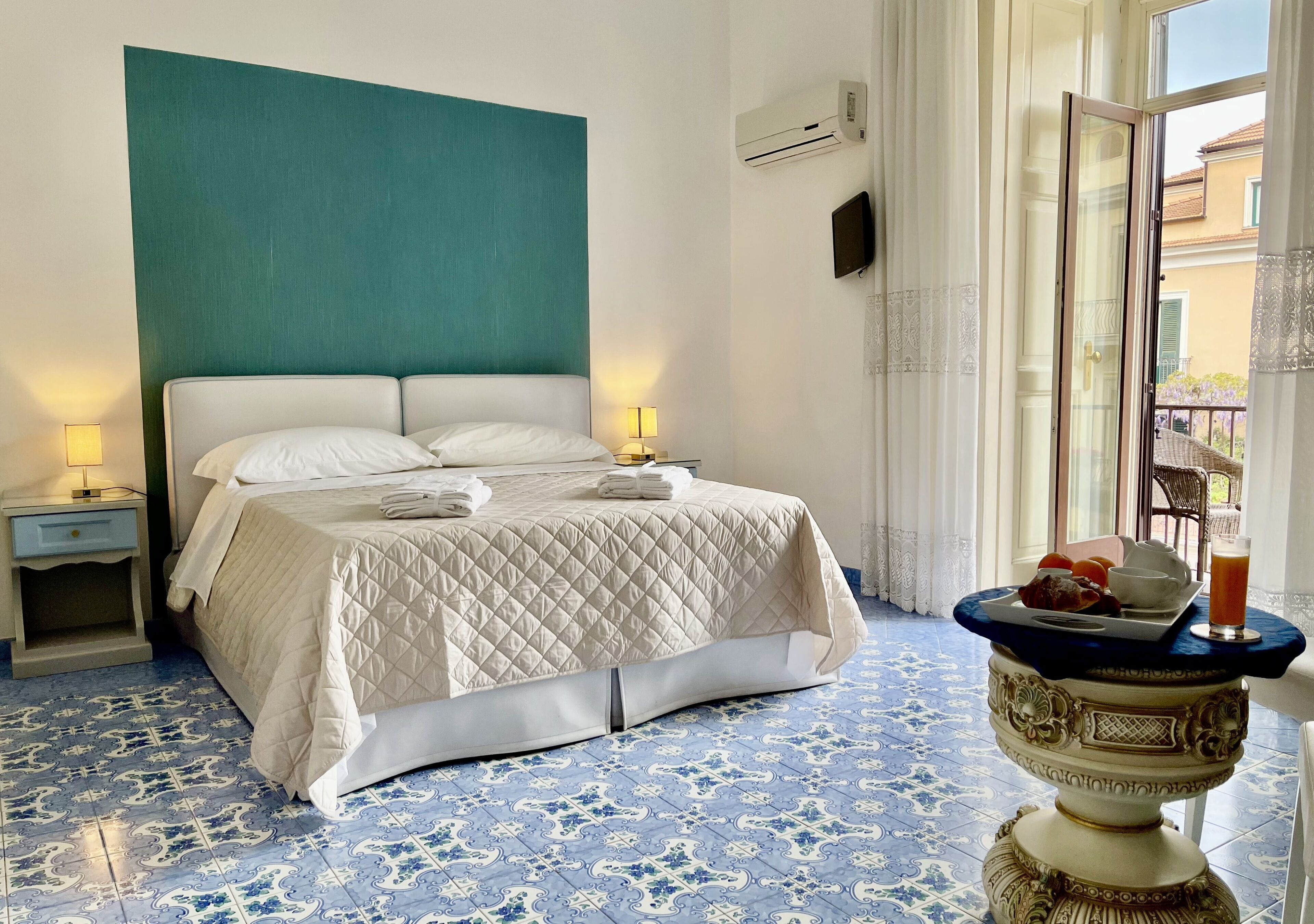 Habitación de hotel con cama, lámparas de noche, una mesita decorativa con una bebida y vistas al exterior.