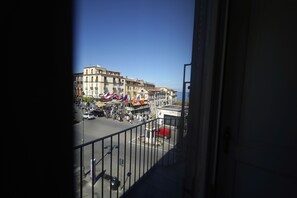 Un balcon donnant sur une rue animée, des immeubles et des drapeaux.
