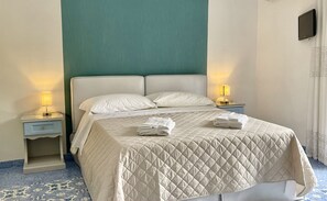 Un lit bien fait, recouvert d'une courtepointe matelassée, avec deux oreillers et une pile de serviettes pliées posée sur le pied de lit. Il y a deux tables de chevet avec des lampes, une de chaque côté du lit.