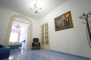 Une pièce comprenant un lit, une chaise, un lustre, un tableau encadré et une porte.
