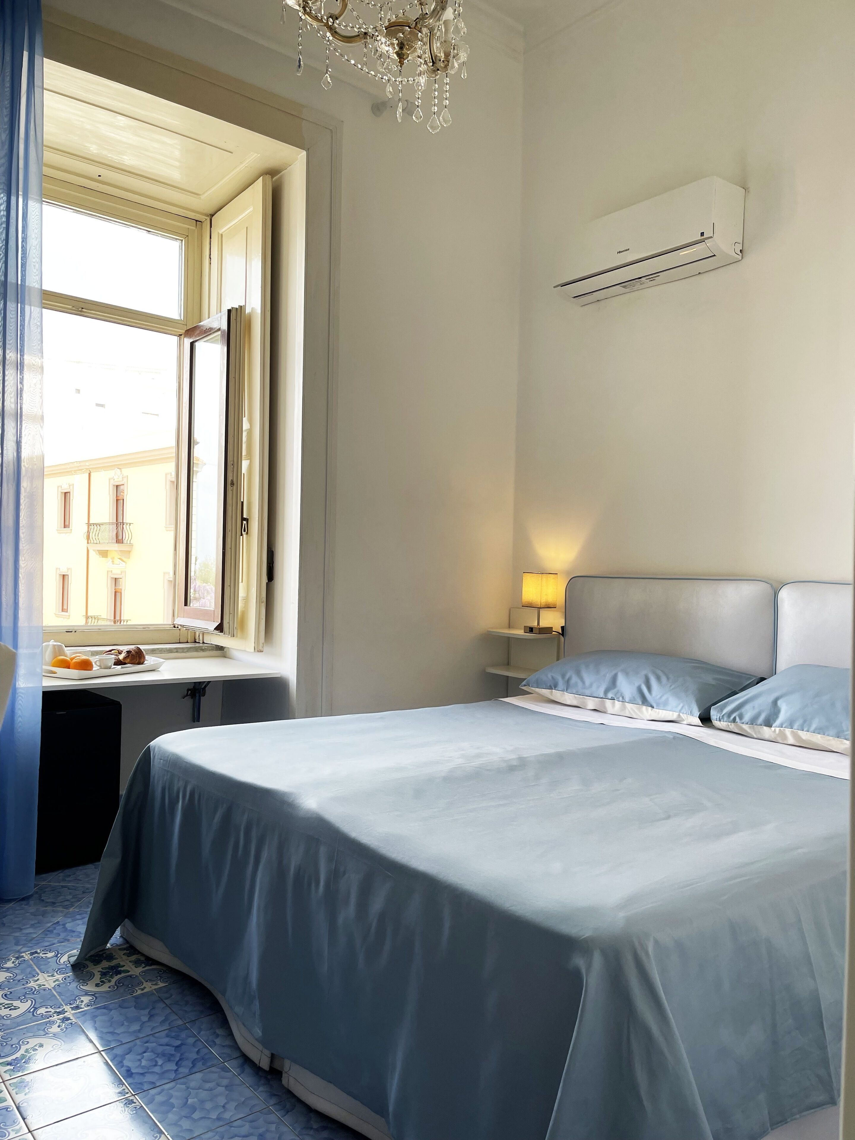 Un dormitorio con cama, ventana, mesita de noche y unidad de aire acondicionado.