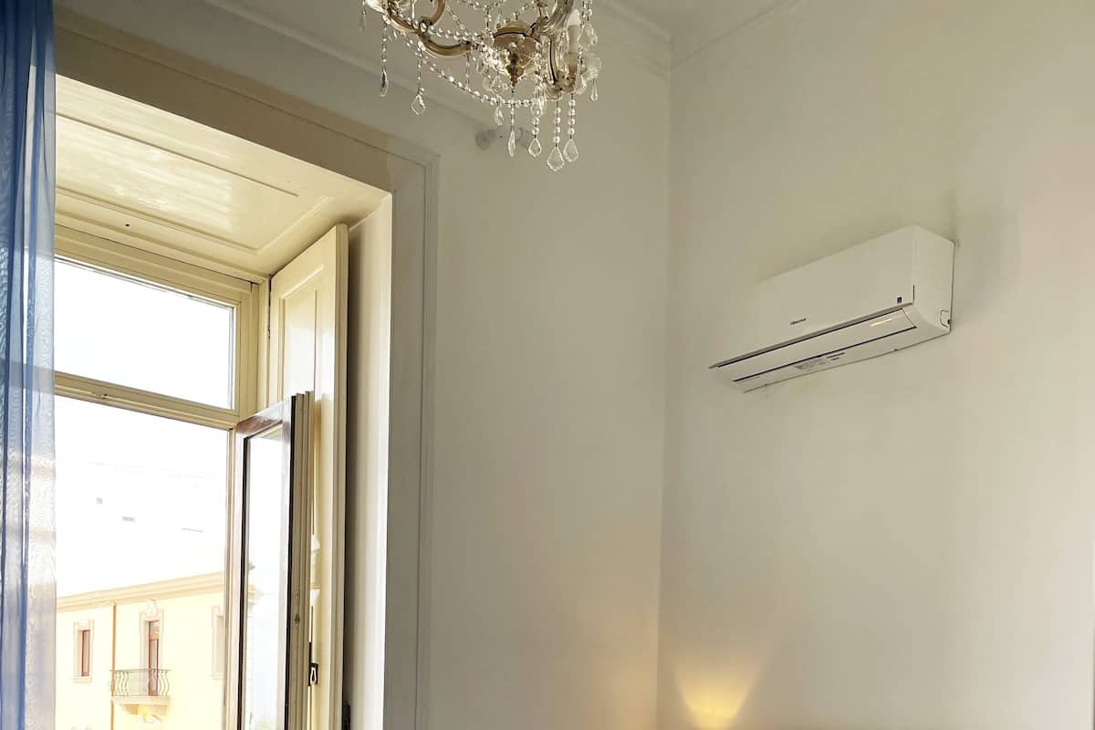 Un dormitorio con cama, ventana, mesita de noche y unidad de aire acondicionado.