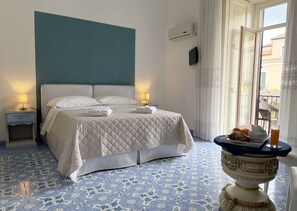 Un lit bien fait, recouvert d’une couverture matelassée, avec deux lampes de chevet et un plateau contenant des croissants et du jus d’orange, posé sur une table.