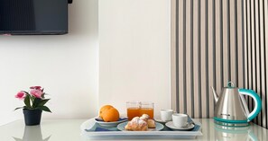 Un plateau de petit-déjeuner avec des viennoiseries, une orange et deux verres de thé sur une table, une théière et une plante en pot aux fleurs roses.