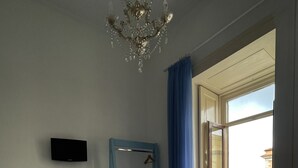 Een hotelkamer met een bed, een bureau met stoel, een televisie, een raam met uitzicht op gebouwen, en een kroonluchter.