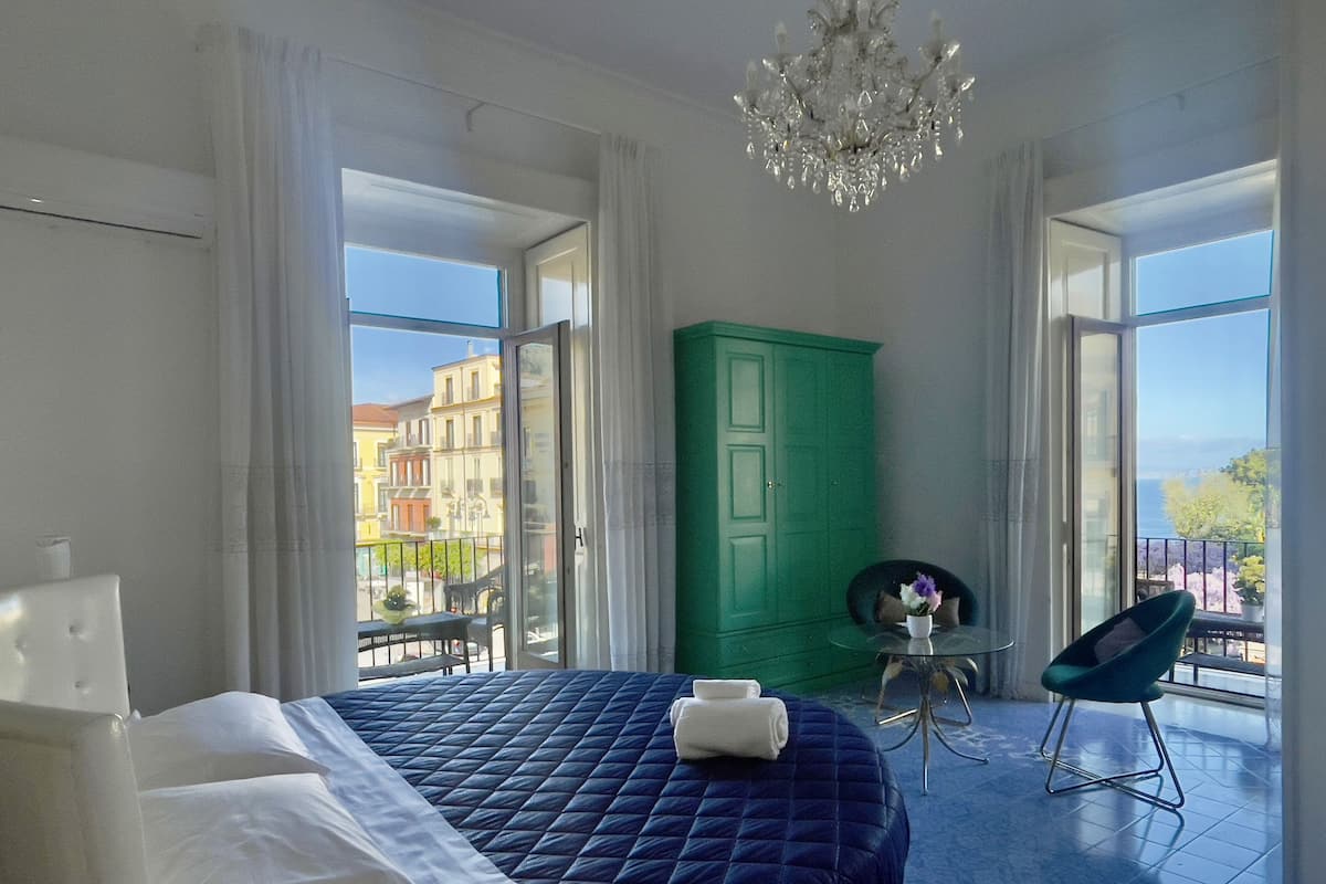 Un dormitorio con una cama, un armario verde, una mesita con un florero y una silla.
