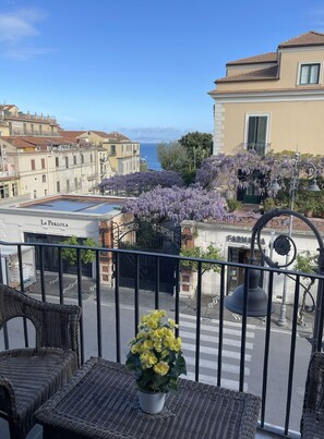 Un balcon agrémenté de meubles en osier, d’une plante en pot et offrant une vue sur la rue et les immeubles.
