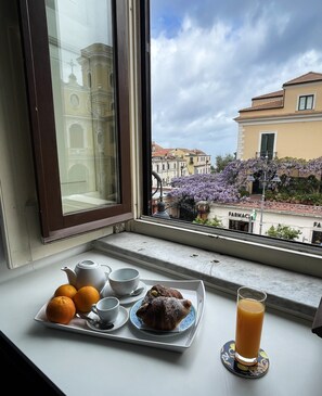 Un plateau de petit-déjeuner avec du jus d’orange, une théière, des tasses et une pâtisserie, posé sur un rebord de fenêtre.