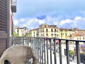 Ein Balkon mit Korbmöbeln, mit Blick auf eine Straße mit Gebäuden und Flaggen.