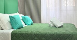 Un lit bien fait, avec une couette verte, des oreillers blancs et une serviette blanche pliée.