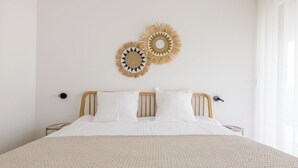 Un lit bien fait, recouvert d’une couverture beige à texture intéressante, avec une tête de lit en bois et deux objets décoratifs fixés au mur.