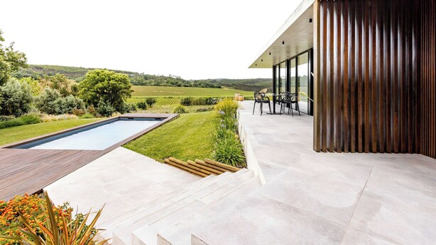 Une terrasse extérieure moderne, dotée d’une piscine, d’une terrasse en bois et d’un espace salon offrant une vue sur la campagne.