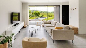 Un salon moderne doté d’une grande porte-fenêtre coulissante donnant accès à une piscine et offrant une vue sur le jardin.