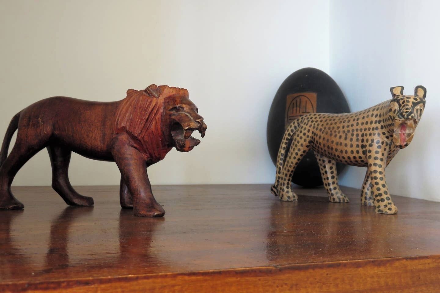 Two wooden animal figurines, one resembling a lion and the other a leopard, placed on a wooden surface.