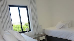 A hotel room with two beds, a bedside table with a lamp, and a window with curtains. - Cape white villa - Family & Friends suite (Cape Town)