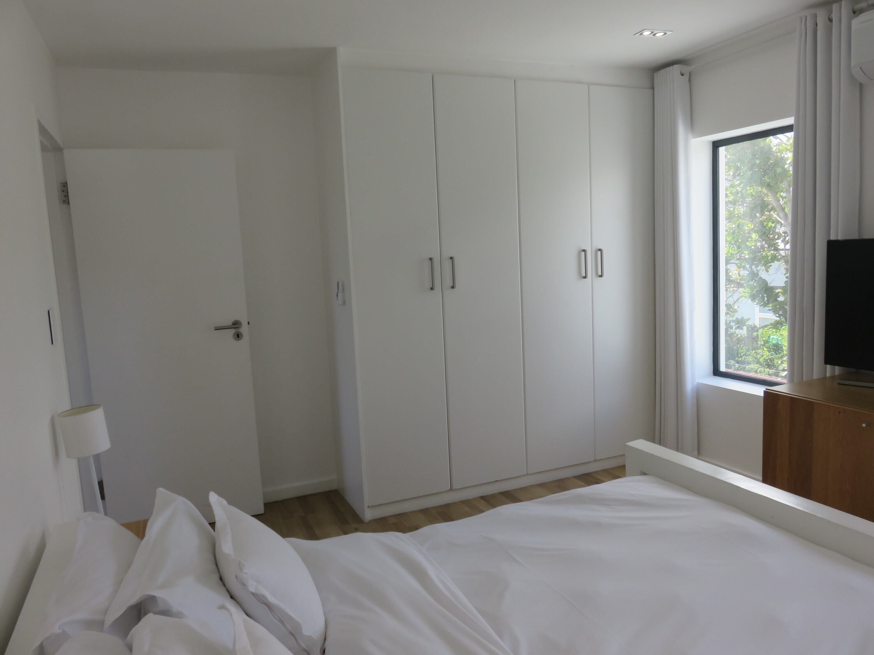 Ein Schlafzimmer mit einem Bett, einem weißen Kleiderschrank und einem Fenster mit Blick auf Bäume.