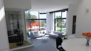 Una sala de estar moderna con una pared de vidrio, un comedor con mesa blanca y un conjunto de sofás.