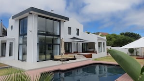 Una casa moderna de dos pisos con piscina, amplios ventanales y mobiliario de exterior.