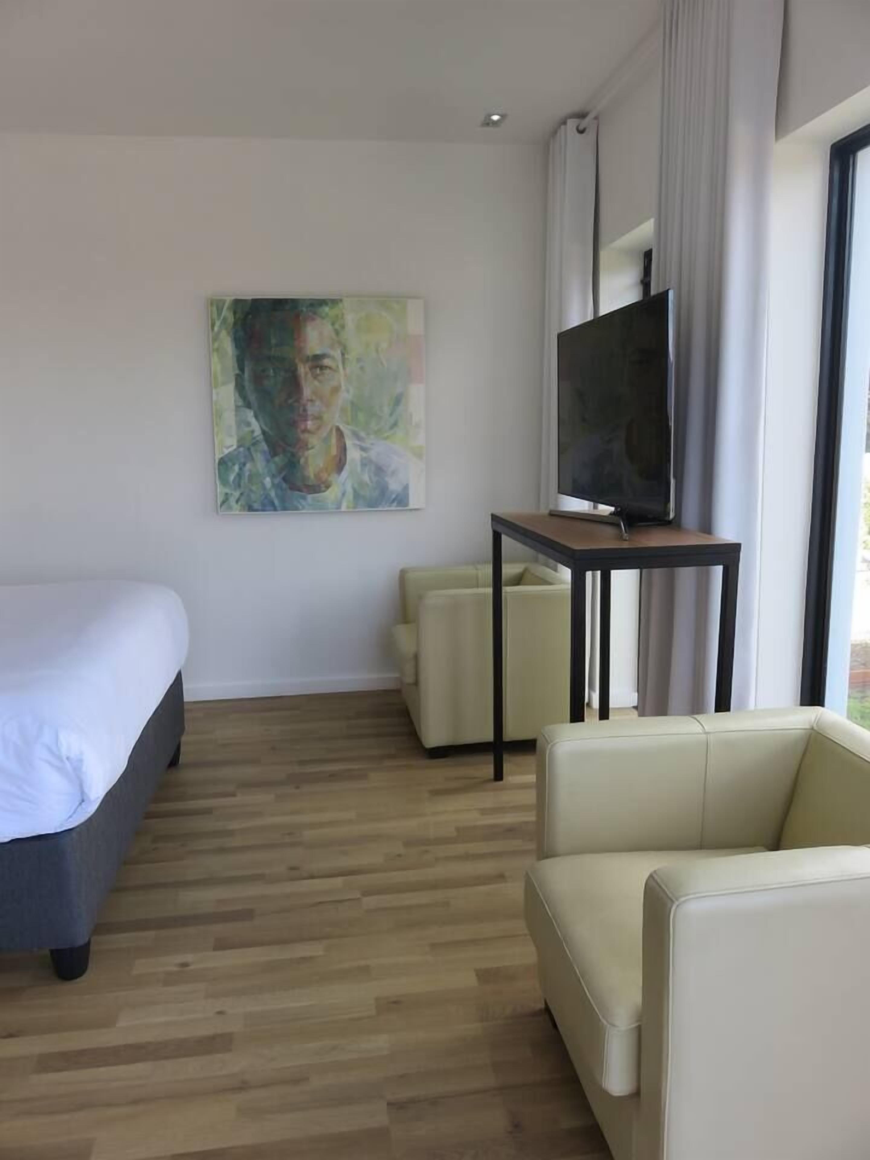 Una habitación de hotel con cama, televisor en un mueble bajo, sofá y un cuadro en la pared.