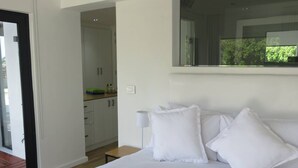 Un dormitorio con una cama grande, ropa de cama blanca, una lámpara de noche y vistas a un balcón.