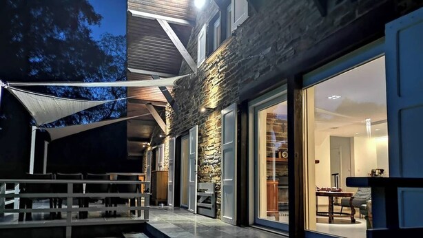 Una casa moderna con fachada de piedra, grandes puertas correderas de vidrio y un interior bien iluminado.