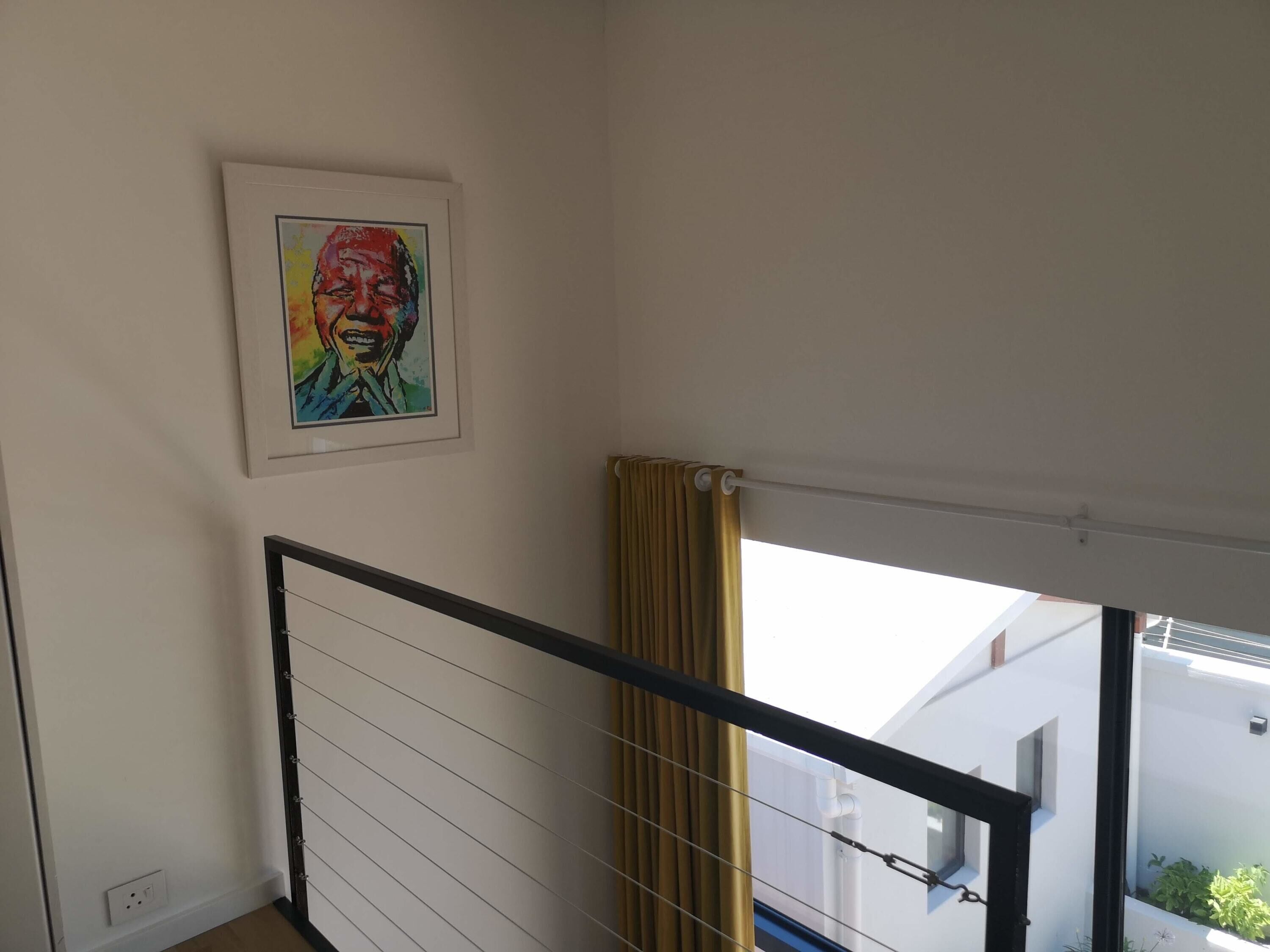 Eine Treppe mit Metallgeländer, ein gerahmtes Kunstwerk an der Wand und ein Fenster mit Vorhang.