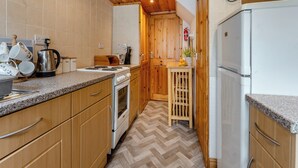 A compact kitchen with wooden cabinets, a stove, a microwave, and a refrigerator. - Carraig Dhubh North - UK47125 (Whiting Bay)
