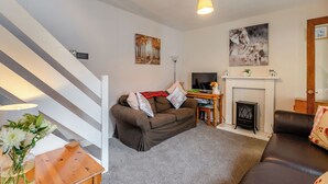 A living room with a brown sofa, a wooden coffee table, a TV, a fireplace, and a staircase. - Carraig Dhubh North - UK47125 (Whiting Bay)