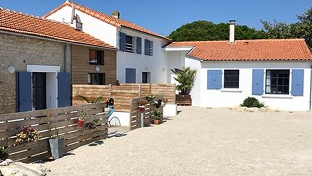 A building with a red-tiled roof, a wooden fence, and a gravel driveway. - L'appartement, Gîte 6. Clos des Aigrettes (ST PIERRE D'OLERON)