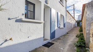 A narrow alleyway with a white building featuring a door and windows. - L'appartement, Gîte 6. Clos des Aigrettes (ST PIERRE D'OLERON)