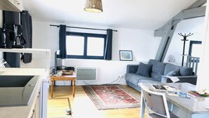 A compact living space with a kitchenette, a sofa, a dining table, and a large window. - L'appartement, Gîte 6. Clos des Aigrettes (ST PIERRE D'OLERON)