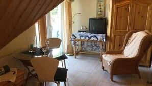 Un saló acollidor amb una taula de menjador, cadires, televisió i una butaca de vimet.