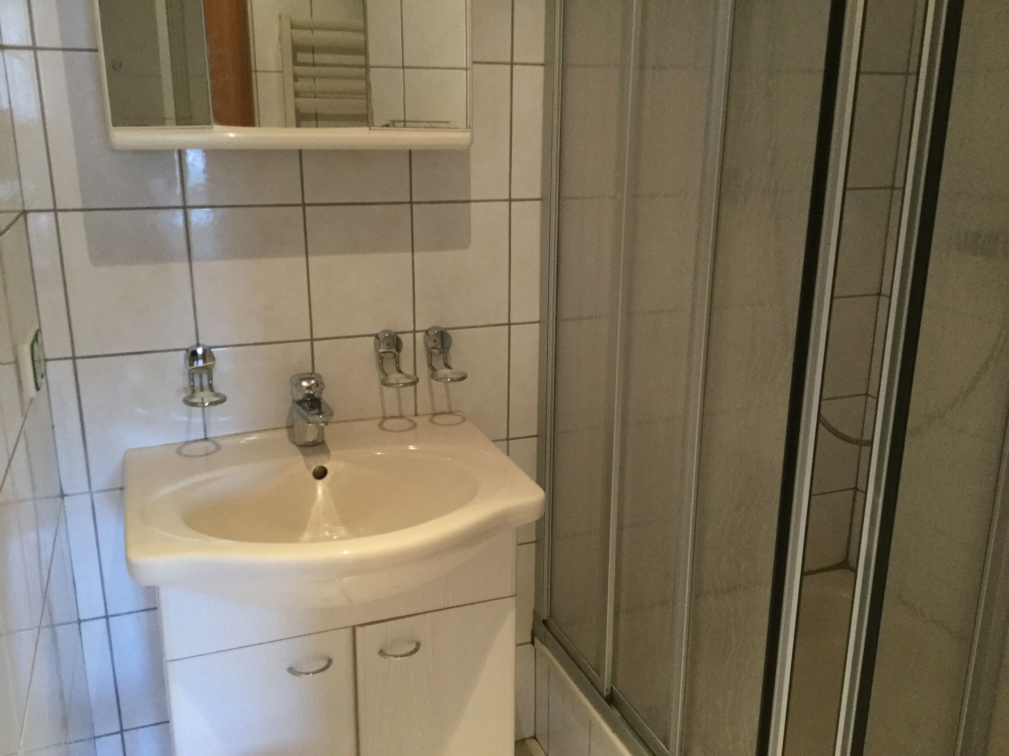 Une salle de bain avec un lavabo blanc, deux robinets et un miroir au-dessus.