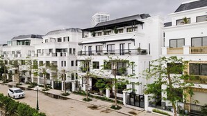 A row of white townhouses with balconies, a paved street, and a parked car. - Pearl Villas Phuong Bai Chay Ha Long   (Bai Chay)