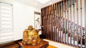 A statue of a laughing Buddha on a wooden platform in a hallway with a wooden partition and a staircase with a metal railing. - Pearl Villas Phuong Bai Chay Ha Long   (Bai Chay)