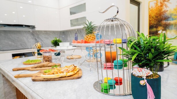 A kitchen counter with various food items, a metal birdcage with colorful macarons, and a potted plant. - Pearl Villas Phuong Bai Chay Ha Long   (Bai Chay)