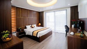 A modern hotel room with a large bed, wooden paneling, a desk with a chair, and a large window with curtains. - Pearl Villas Phuong Bai Chay Ha Long   (Bai Chay)