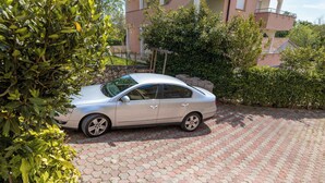 A silver sedan parked on a paved driveway with a stone wall and greenery in the background.