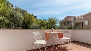 An outdoor patio with two white chairs and a table, surrounded by a low wall and trees.