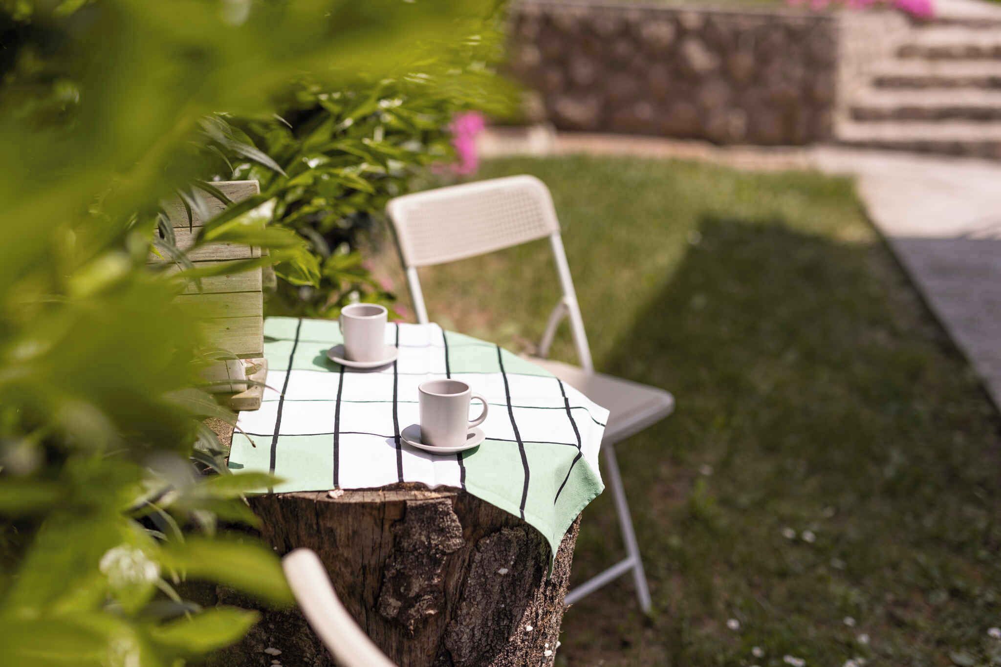 A table set outdoors with a checkered tablecloth, two white cups, and saucers.