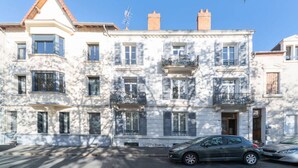 Un immeuble à plusieurs étages, de style architectural classique, doté de balcons avec des garde-corps en métal et d’une entrée centrale.