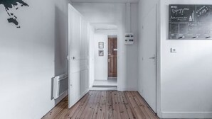 Un couloir doté d’un plancher en bois, de murs blancs et d’une porte donnant sur une autre pièce.