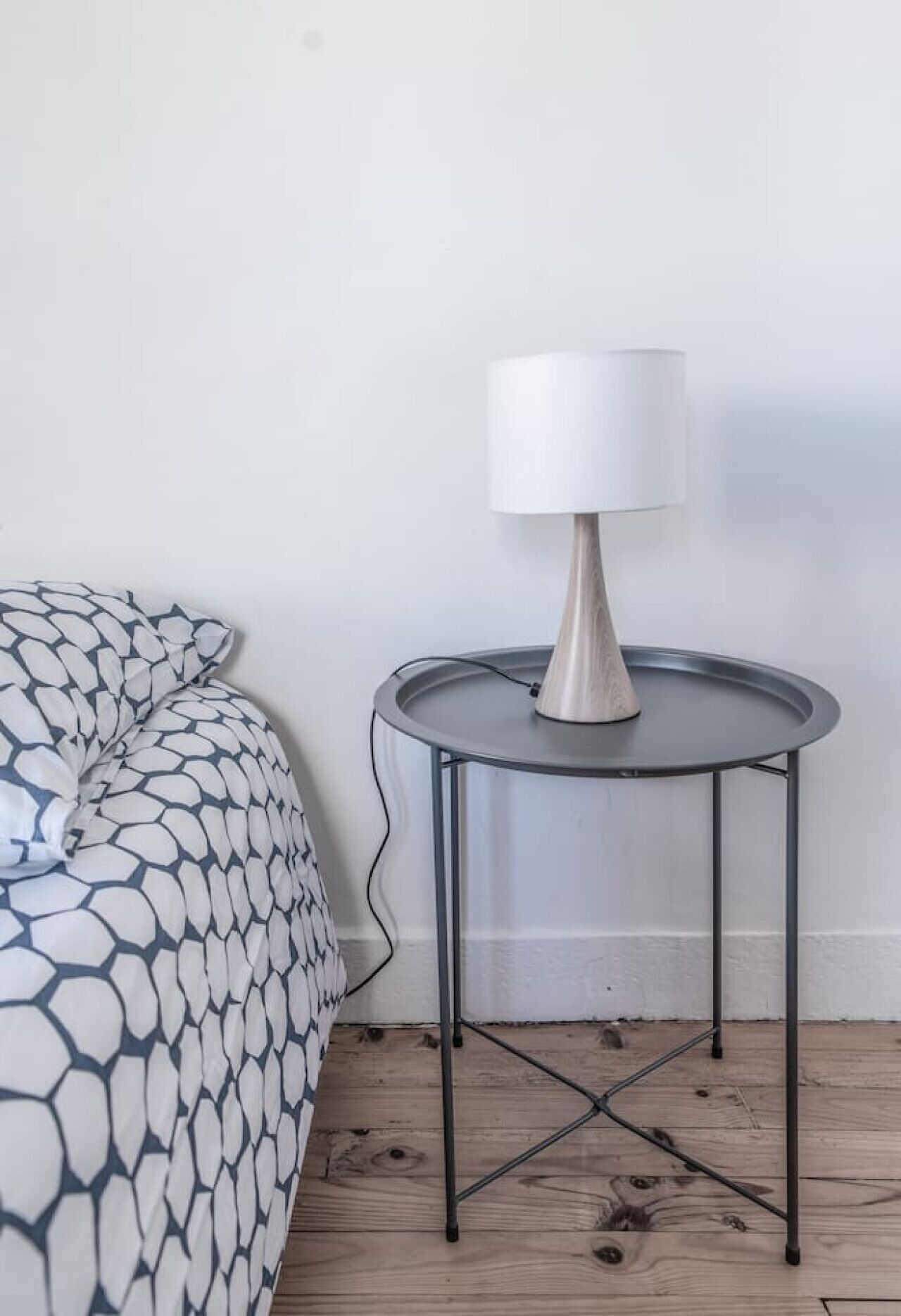 A bed with a patterned duvet and a small round table with a lamp beside it.