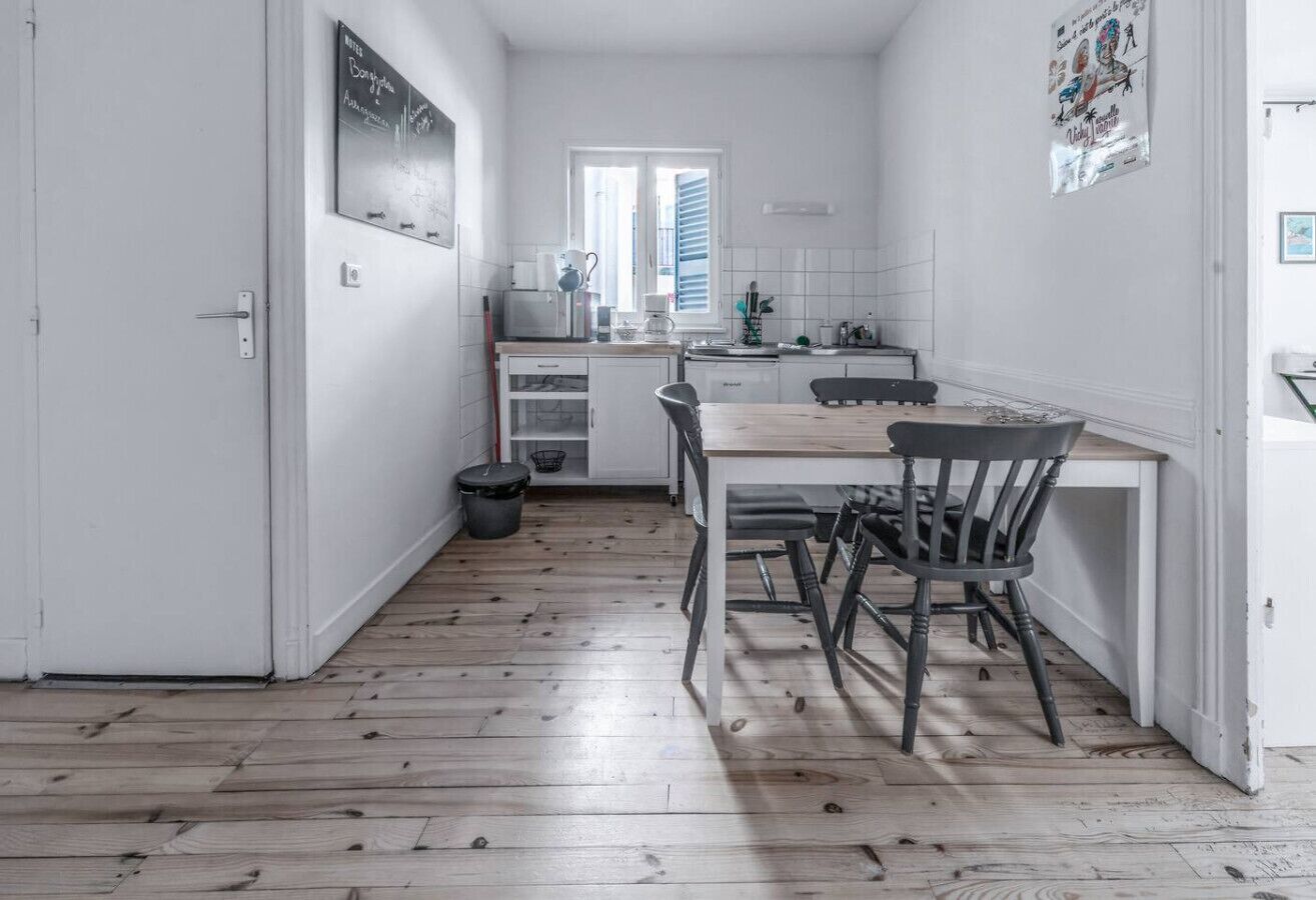 Une cuisine compacte comprenant une table et des chaises, une fenêtre avec des stores et un crédence carrelée blanche.