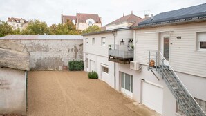 A residential building with a gravel driveway, a small fenced area, and a staircase leading to a balcony. - Quiet and cosy apartment, free parking (Vichy)