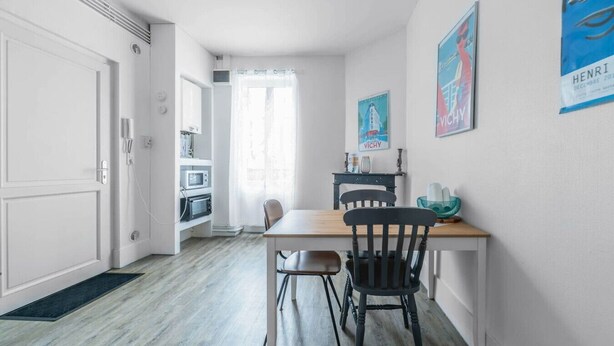 A compact kitchen with a wooden table and chairs, a microwave, and a window with sheer curtains. - Quiet and cosy apartment, free parking (Vichy)
