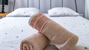 A neatly made bed with two rolled towels, a map on the wall, and a simple nightstand with a lamp. - Quiet and cosy apartment, free parking (Vichy)
