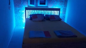 Een bed met hoofdbord, kussens en opgevouwen dekens in een kamer met stenen muren en een raam.